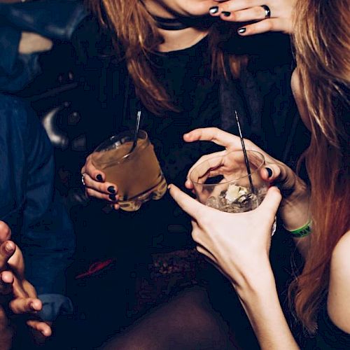 People are holding drinks and socializing, with one person seen laughing. The scene appears to be lively and possibly taken at a party or social gathering.