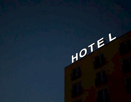 An illuminated "HOTEL" sign on the top corner of a building against a dark sky, but the letter "L" is slightly tilted.