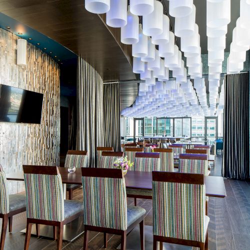 This image shows a modern dining area with colorful striped chairs, a flat-screen TV on the wall, and unique cylindrical ceiling lights ending the sentence.